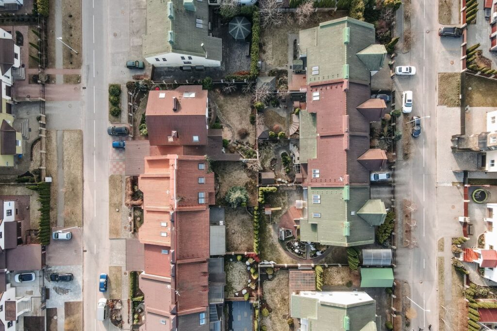 Aerial drone shot of a residential area with houses, streets, and parked cars.